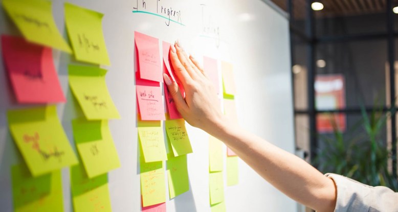 Close up of someone placing a post it note onto a whiteboard