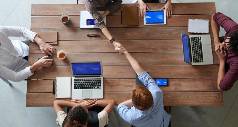 Overhead view of a group of people meeting across a desk, two people on opposite sides are shaking hands