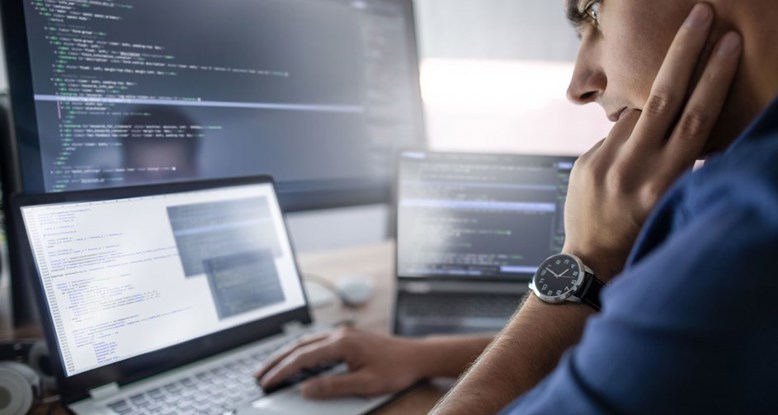 Photograph of someone working at a laptop with other computer screens around them