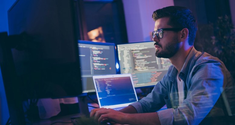 Photograph of someone working in a softly lit office surounded by multiple screens