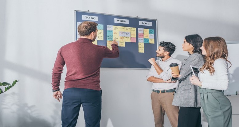 Photograph of a team gathered around a planning board reviewing tasks