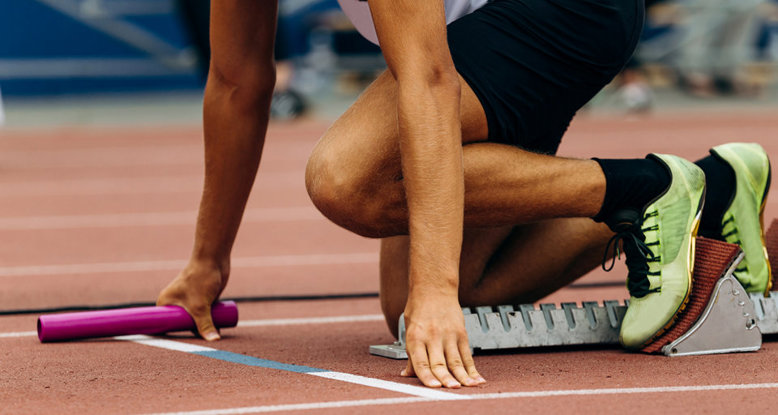 Photograph of an athlete poised in the starting blocks holding a baton